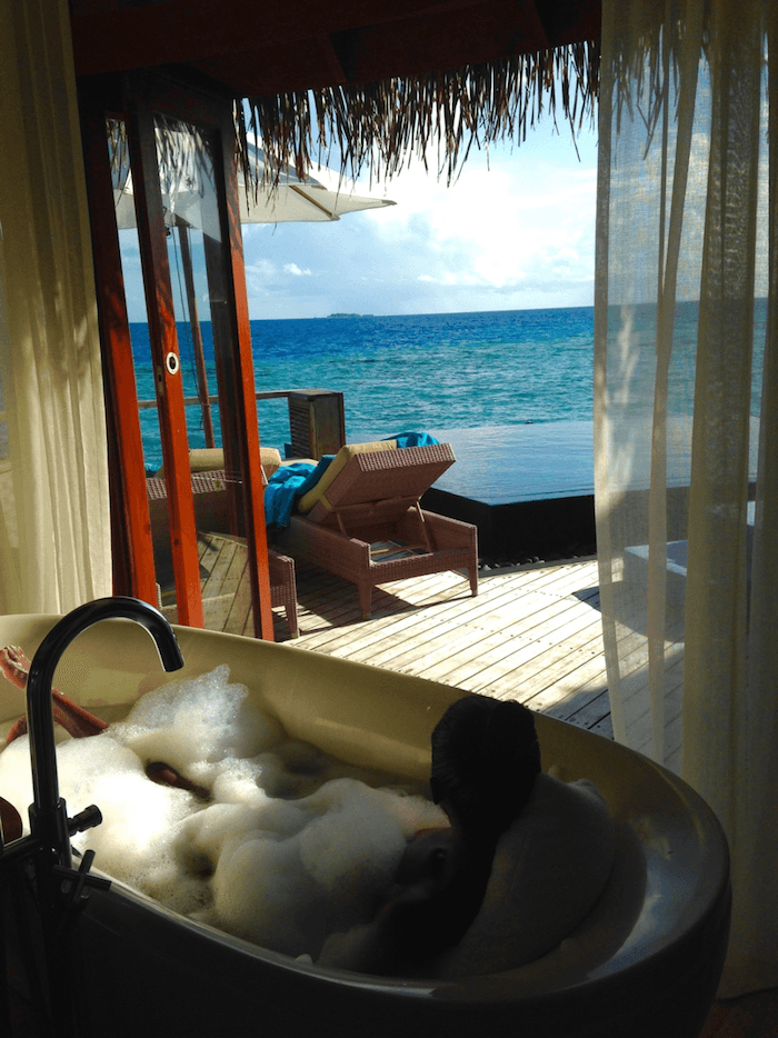 woman taking bubble bath in front of open doors to the ocean