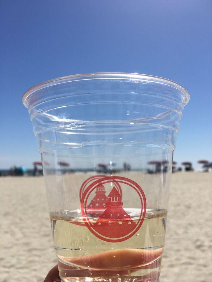 a plastic cup filled with Prosecco with the beach in background