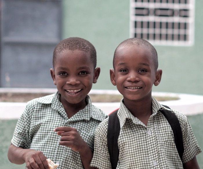 two children smiling, one with backpack and one with sandwich