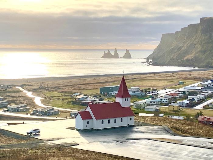 a church in Vik with a red roof and steeple overlooking the water