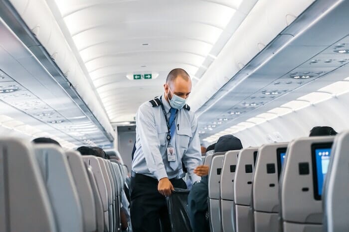 masked flight attendant collecting trash